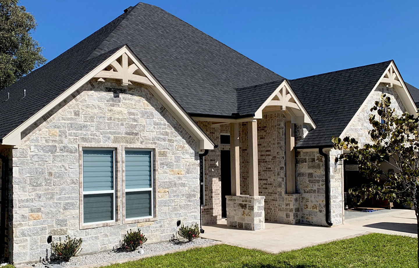 A white stone one story home with white oak beams and gable brackets.
