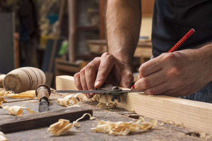 Man marking wood carving with wood tool and a red pencil.